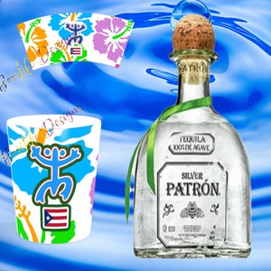May include: A clear glass bottle of Patron Silver Tequila with a green ribbon and cork stopper. The bottle is labeled "Tequila 100% de Agave" and "Silver Patron". The bottle is sitting on a blue and white background with a shot glass and a cup with a Puerto Rican flag and a Coqui frog design.