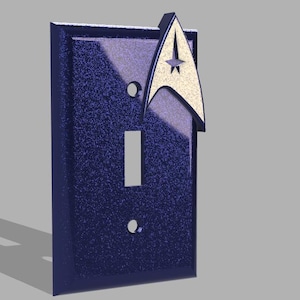 May include: A dark blue light switch cover with a white Starfleet insignia. The switch cover has a textured surface.