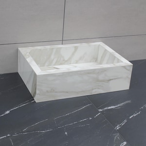 Könnte beinhalten: Ein rechteckiges Waschbecken aus weißem Marmor mit grauer Maserung. Das Waschbecken steht auf einer dunkelgrauen Arbeitsplatte mit weißer Maserung. Der Hintergrund ist eine hellgraue Wand. Das Waschbecken ist ein modernes Badezimmerobjekt.