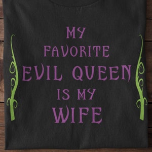 Op de afbeelding: Zwart T-shirt met de tekst "My favorite evil queen is my wife" in paars en groene wijnstokken aan de zijkanten.