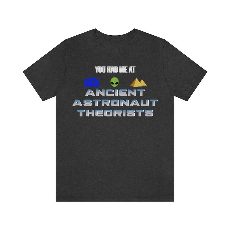 May include: Dark grey t-shirt with the text "You had me at Ancient Astronaut Theorists" in a silver metallic font. The text is accompanied by three icons: a blue pyramid, a green alien, and a gold pyramid.