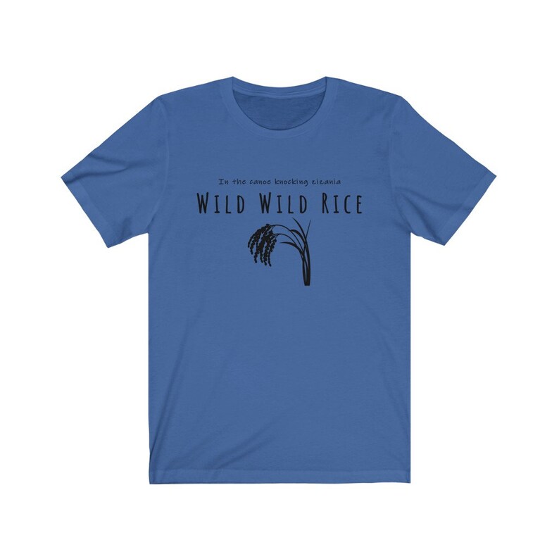 Puede incluir: Una camiseta azul con el texto "In the canoe knocking bizania WILD WILD RICE" y una silueta negra de un tallo de arroz.
