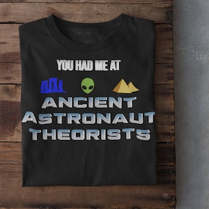 May include: Black t-shirt with the text "You had me at Ancient Astronaut Theorists" in white with blue and yellow icons of a pyramid, an alien, and a building.