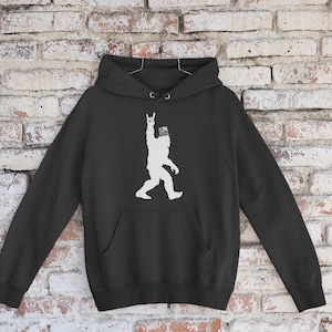 May include: Black hooded sweatshirt with a white silhouette of a Bigfoot giving the rock and roll hand gesture.