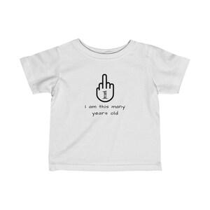 K&ouml;nnte beinhalten: Wei&szlig;es T-Shirt f&uuml;r Kleinkinder mit einem schwarzen Mittelfinger, in dem die Zahl 1 steht. Der Text darunter lautet "Ich bin so viele Jahre alt".