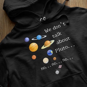 Könnte beinhalten: Schwarzer Hoodie mit einer weißen Grafik der Planeten unseres Sonnensystems. Der Text lautet "We don't talk about Pluto... no... no... no..." mit einem Ausrufezeichen und einer kleinen Grafik von Pluto.