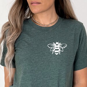 May include: A dark green t-shirt with a white bee graphic on the front. The shirt is made of a soft, comfortable material and has a relaxed fit.