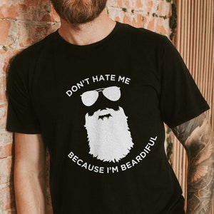 May include: A black t-shirt with a white graphic of a bearded man wearing sunglasses and the text "Don't hate me because I'm beardful".