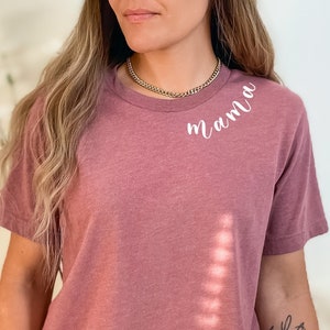 K&ouml;nnte beinhalten: Ein bauchfreies T-Shirt in Mauve mit dem Wort "mama" in Wei&szlig; auf der linken Schulter. Das Shirt ist aus einem weichen, bequemen Stoff.