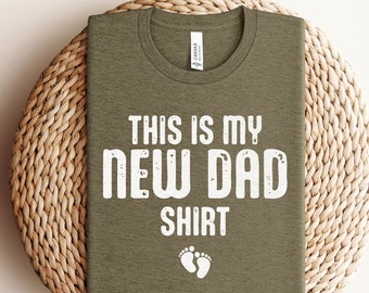 May include: A green t-shirt with the text "This is my new dad shirt" in white with a pair of white baby footprints below the text.