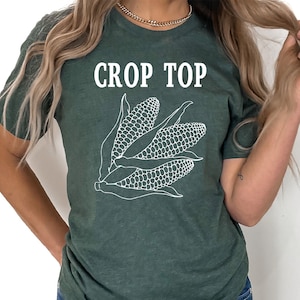 Op de afbeelding: Een donkergroen crop top met een witte omtrek van maïs aan de voorkant. De tekst "Crop Top" is in wit boven de maïs gedrukt.