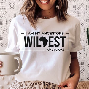 Peut inclure: T-shirt blanc avec un motif noir qui dit "I am my ancestors wildest dreams" avec un contour du continent africain. La personne portant le t-shirt tient une tasse blanche.