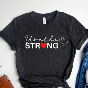 May include: Heather dark gray t-shirt with the text "Uvalde STRONG" in white with a red heart and an outline of the state of Texas.