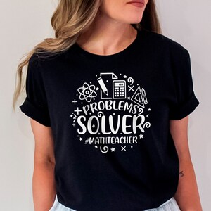 May include: Black t-shirt with white text that reads "Problems Solver #MathTeacher" with math-related icons surrounding the text.