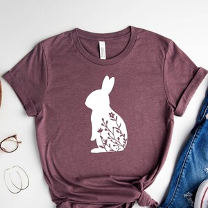 May include: A mauve t-shirt with a white silhouette of a rabbit with floral details.