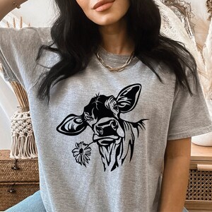 May include: A heather grey t-shirt with a black and white illustration of a cow's head with a flower in its mouth.