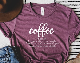 May include: A maroon t-shirt with the word "coffee" written in white cursive lettering. The definition of coffee is written below in white text: "(n) [ko-fe] A magical, dark, liquid made of freshly ground heaven and gold. A perfect excuse to take a break."