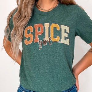 May include: A green t-shirt with the text "Spice girl" in a retro font with orange, yellow, and brown colors.