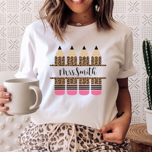 May include: White t-shirt with a design of three pencils with leopard print and the text "Mrs. Smith".
