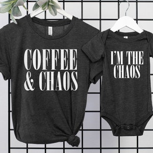 May include: A dark heather grey t-shirt with the text "COFFEE & CHAOS" in white. A matching dark heather grey baby onesie with the text "I'M THE CHAOS" in white.