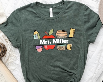 May include: A green t-shirt with a design of a red apple, a pencil, a coffee cup, and a ruler. The text "Mrs. Miller" is printed on the shirt.