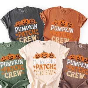 Peut inclure: Cinq t-shirts à manches courtes de couleurs variées : gris, orange, vert, crème et marron. Chaque t-shirt affiche le texte "PUMPKIN PATCH CREW" avec des motifs de citrouilles, parfait pour l'automne et Halloween.