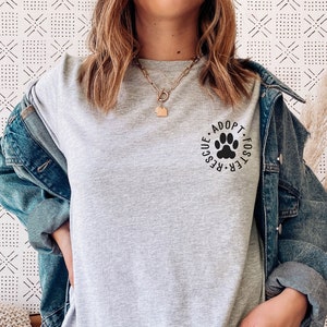 May include: A heather grey t-shirt with a black paw print graphic and the text "Foster-Rescue-Adopt-Fosters" around the paw print.
