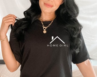 Könnte beinhalten: Eine Frau trägt ein schwarzes T-Shirt-Kleid mit dem Text "HOME GIRL" und einer Hausgrafik. Sie trägt goldene Halsketten und ein goldenes Armband.