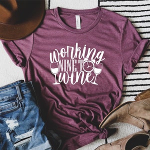 May include: A maroon t-shirt with the text "working nine to wine" in white lettering. The text includes a clock and two wine glasses.