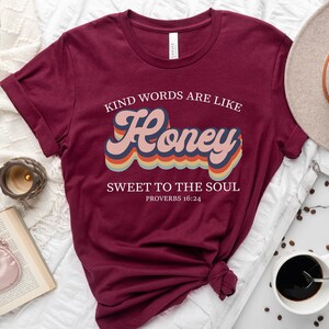 May include: Maroon t-shirt with a retro-style graphic that says "Kind words are like Honey Sweet to the Soul Proverbs 16:24".
