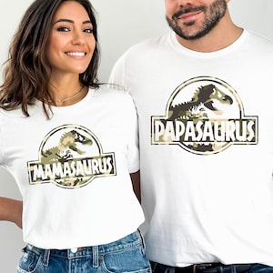 May include: White t-shirts with a camouflage dinosaur graphic and the text "Mamasaurus" and "Papasaurus".