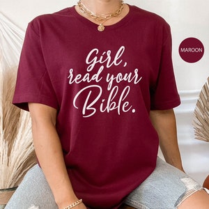 Pode incluir: Uma camiseta vinho com o texto "Girl, read your Bible." impresso em branco.