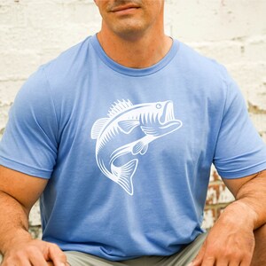 May include: A light blue t-shirt featuring a white graphic of a bass fish leaping out of the water.