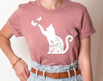 May include: A heather mauve t-shirt with a white graphic of a cat with butterflies and floral details. The text "HEATHER MAUVE" is displayed in a circle above the shirt.
