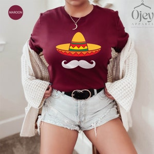 May include: A maroon t-shirt with a white mustache and a colorful sombrero graphic. The text "Ojay Apparel" is visible in the top right corner of the image.