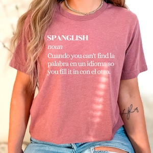 Puede incluir: Una camiseta color malva con la palabra "SPANGLISH" definida como "Cuando you can't find la palabra en un idioma so you fill it in con el otro."