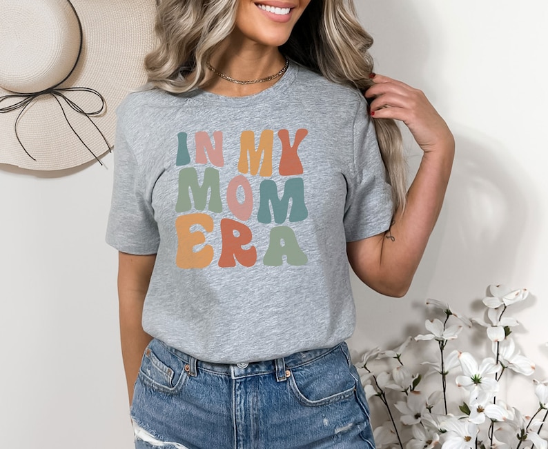 May include: A gray t-shirt with the text "In My Mom Era" in colorful, retro-style lettering.