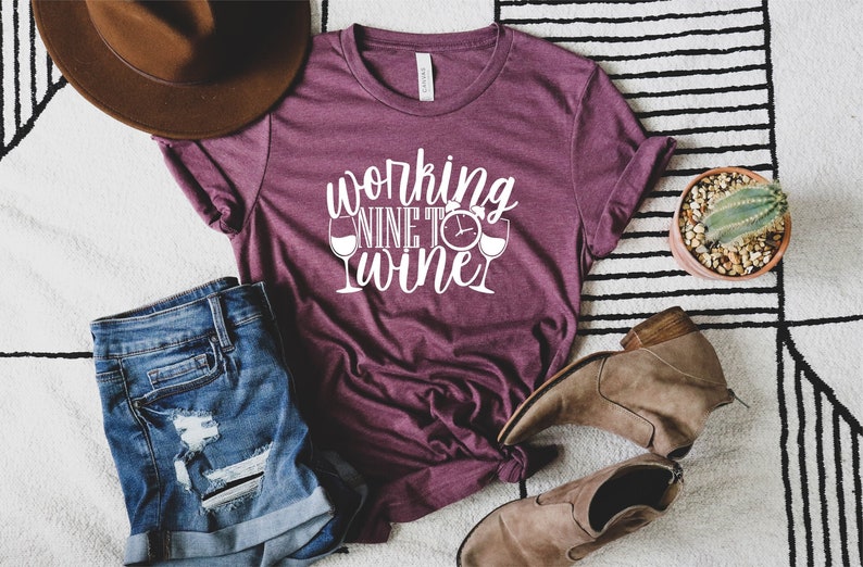 May include: A maroon t-shirt with the text "working nine to wine" in white lettering. The text includes a clock and two wine glasses.