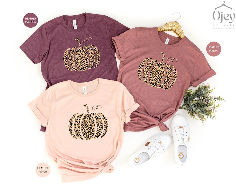 May include: Three t-shirts with a leopard print pumpkin design. The shirts are in heather maroon, heather mauve, and heather peach.