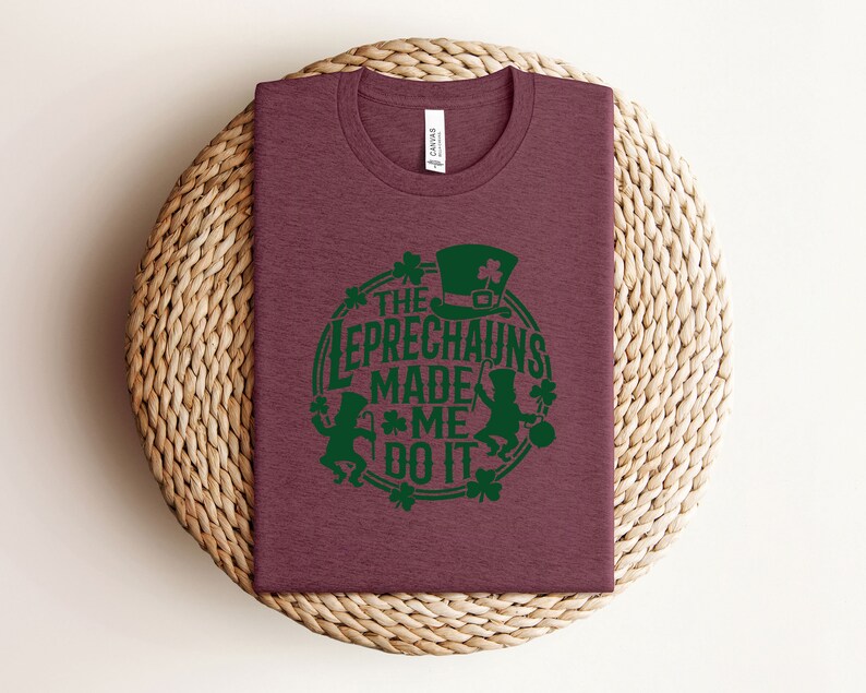May include: A maroon t-shirt with a green graphic design that says "The Leprechauns Made Me Do It". The graphic features two leprechauns with green hats and green shamrocks.