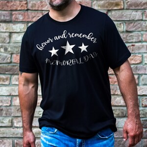 以下が含まれることがあります： 白い文字で「honor and remember MEMORIAL DAY」と書いてある、3つの白い星がついた黒いTシャツ