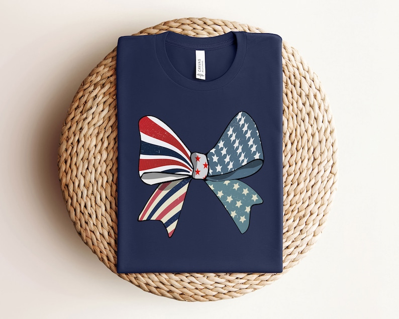 May include: A navy blue t-shirt with a red, white, and blue bow design. The bow is made of fabric with a stars and stripes pattern.