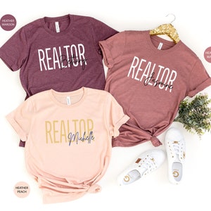 Peut inclure: Trois t-shirts en coton m&eacute;lang&eacute; avec le mot "REALTOR" et un nom imprim&eacute; sur chacun. Les t-shirts sont en coloris heather maroon, heather mauve et heather peach.
