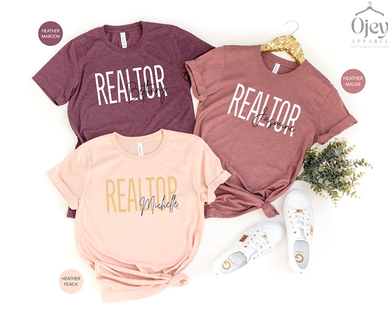 Peut inclure: Trois t-shirts en coton m&eacute;lang&eacute; avec le mot "REALTOR" et un nom imprim&eacute; sur chacun. Les t-shirts sont en coloris heather maroon, heather mauve et heather peach.