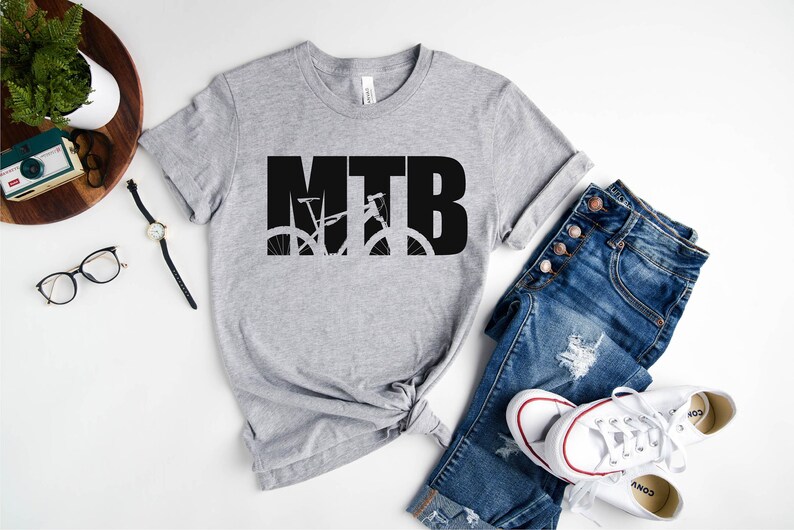 Puede incluir: Una camiseta gris con la palabra "MTB" en letras negras, con una silueta de una bicicleta de monta&ntilde;a dentro de las letras.