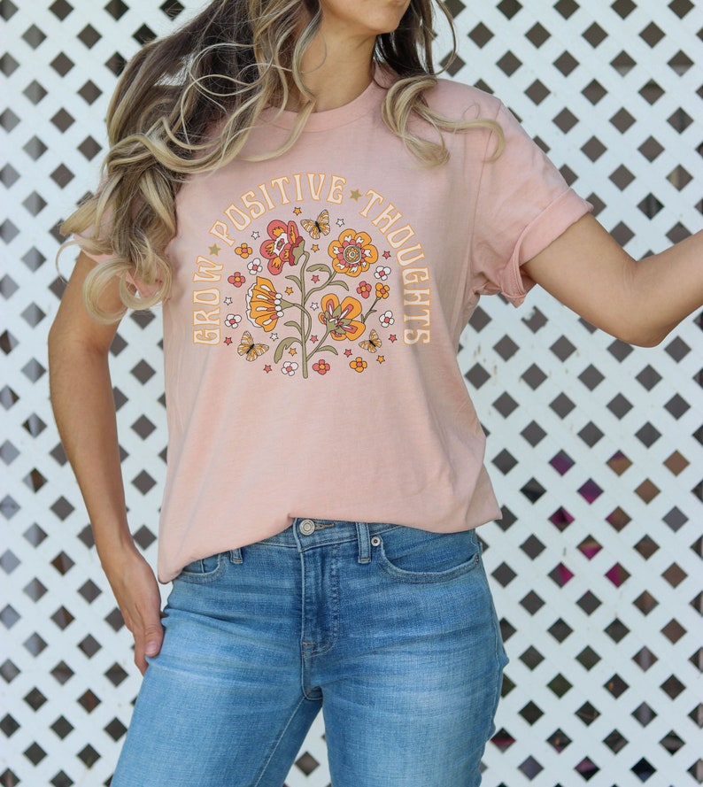 May include: A pink t-shirt with a floral design and the text "Grow Positive Thoughts" in a retro font.