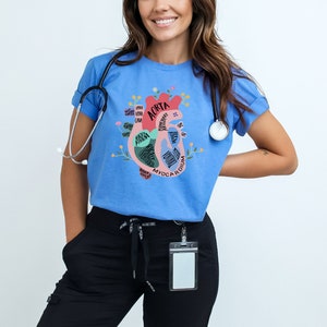 May include: A light blue t-shirt with a graphic of a heart with the anatomy of the heart labeled. The heart is pink and red with green and blue accents. The text on the shirt reads "Aorta, Myocardium, Pulmonary Valve, Right Atrium, Left Atrium, Right Ventricle, Left Ventricle, Tricuspid Valve, Mitral Valve, Aortic Valve, Pulmonary Artery, Pulmonary Vein, Superior Vena Cava, Inferior Vena Cava".