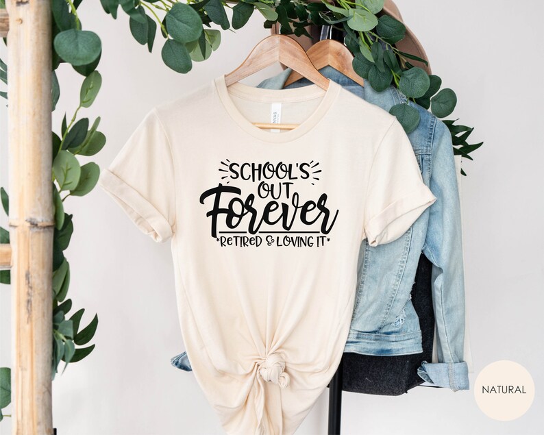 Puede incluir: Una camiseta beige con el texto "School's Out Forever - Retired & Loving It" impreso en negro.