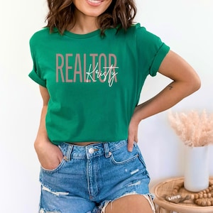 Peut inclure: Un t-shirt vert avec le texte "REALTOR" en rose et le nom "Kristy" en &eacute;criture blanche.