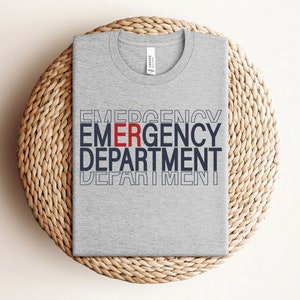 Może przedstawiać: Szary t-shirt z nadrukiem "EMERGENCY DEPARTMENT" w kolorze granatowym i czerwonym.